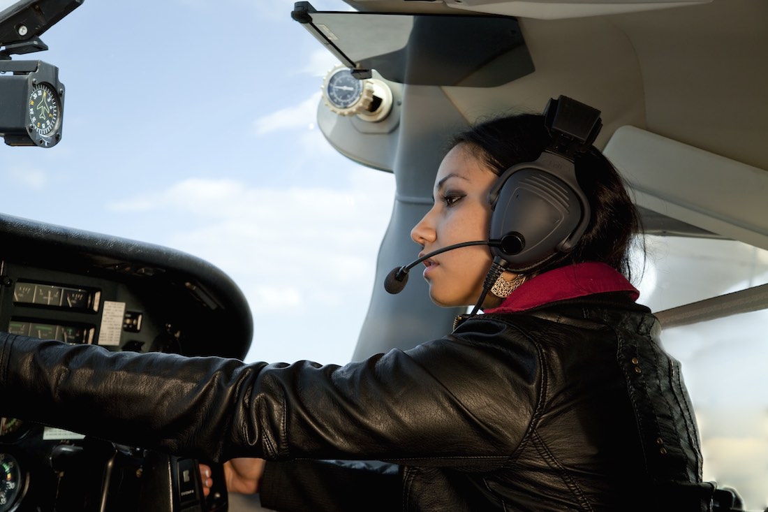 A woman is flying an airplane and messing with the instruments