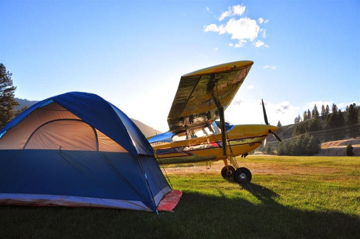 A Cessna 180 Skywagon against a sunrise, with a camping tent
