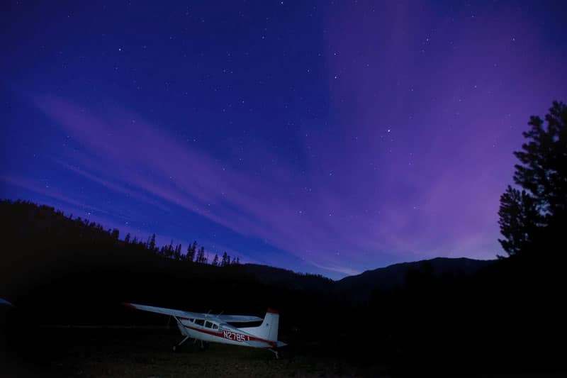 A Cessna 185 Skywagon at a backcountry airstrip with the night sky