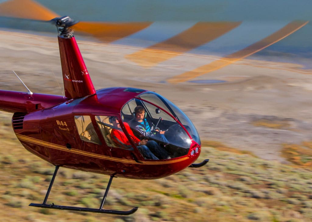 Robinson R44 Helicopter in flight by the shore of a lake