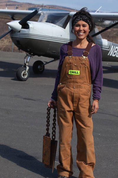 Ariel Tweto standing on a runway in front a tailldragger airplane.