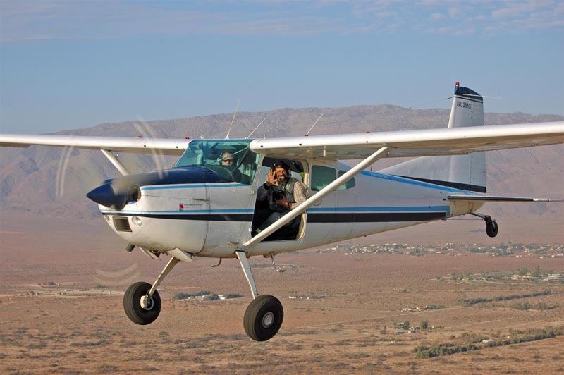 A Cessna 185 Skywagon flying with the door off to take photographs